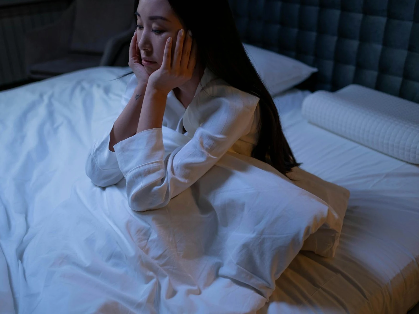 어두운 침실 침대 위에 앉아 양손으로 얼굴을 받친 채 깨어 있는 여성, 잠들지 못한 한밤중 불면증 장면